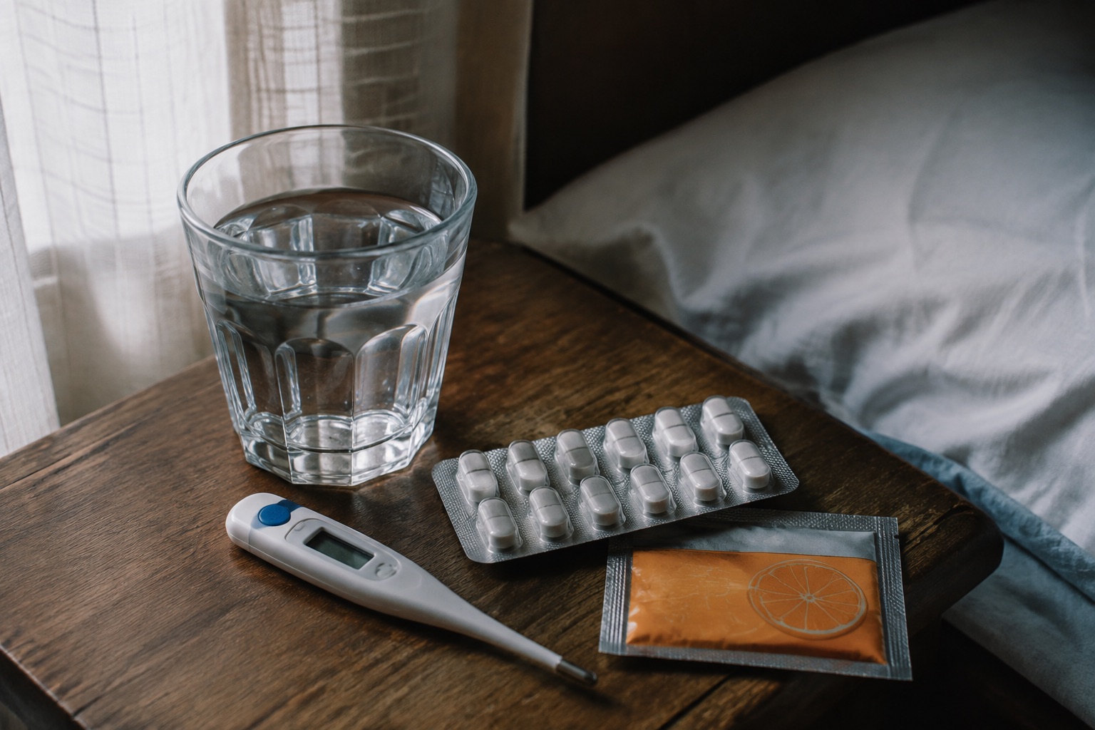 Bedside table: thermometer, paracetamol packet, water glass, rehydration sachet